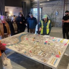 Community members engage in city planning discussion around a detailed urban model.