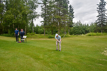 Golfer preparing to swing on a lush green golf course with spectators enjoying the game.
