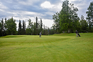 Serene golf course with lush green greens, golfers, and tranquil nature setting under cloudy skies.
