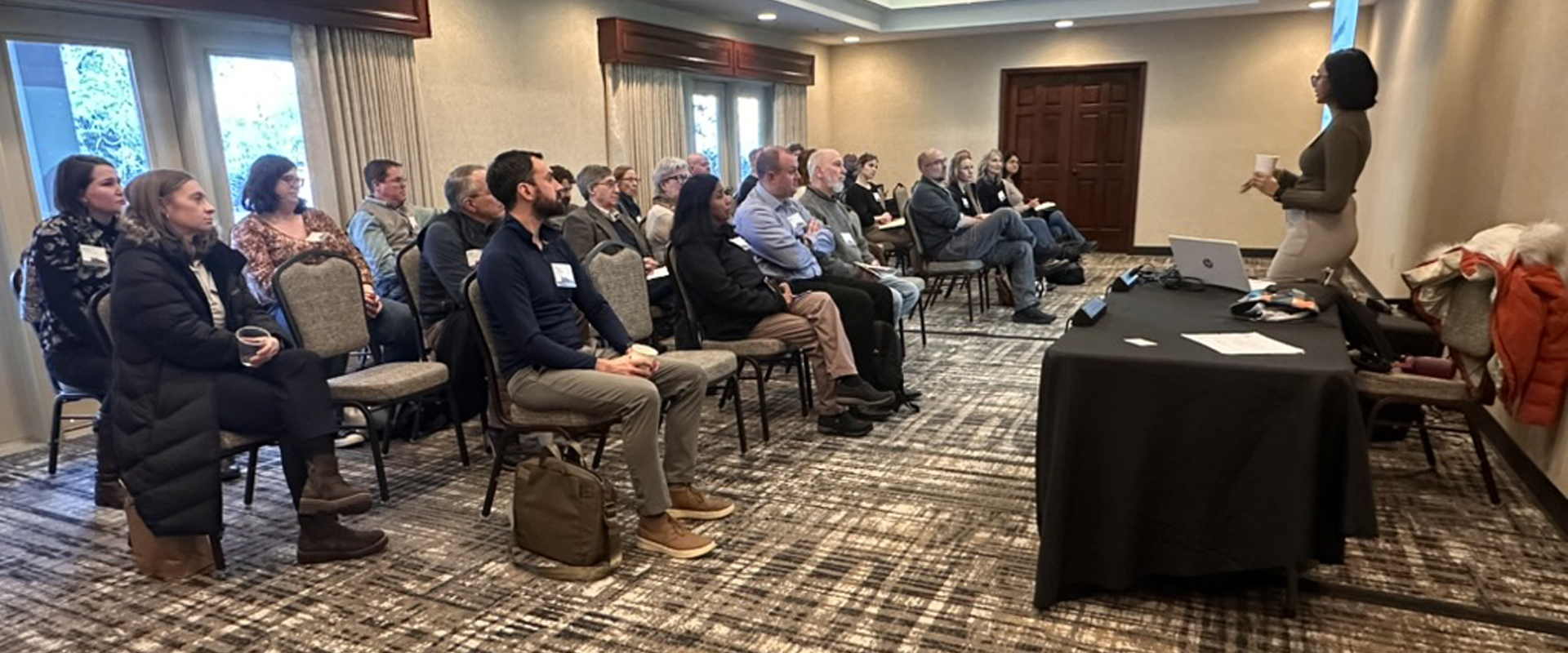 Engaged audience at a professional seminar in a well-lit conference room with a speaker.